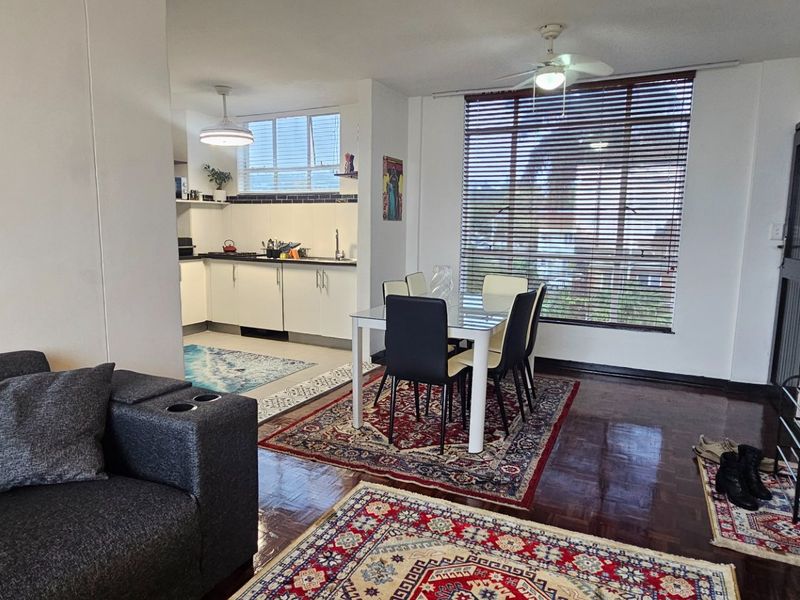 Open-plan living and dining area featuring parquet flooring, a ceiling fan, and an adjoining kitchen with built-in cabinetry.