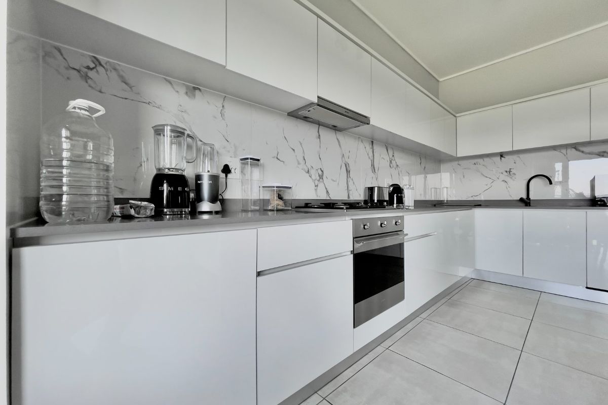 Modern kitchen featuring sleek white cabinetry, marble-look splashbacks, integrated appliances, and high-quality tiled flooring.