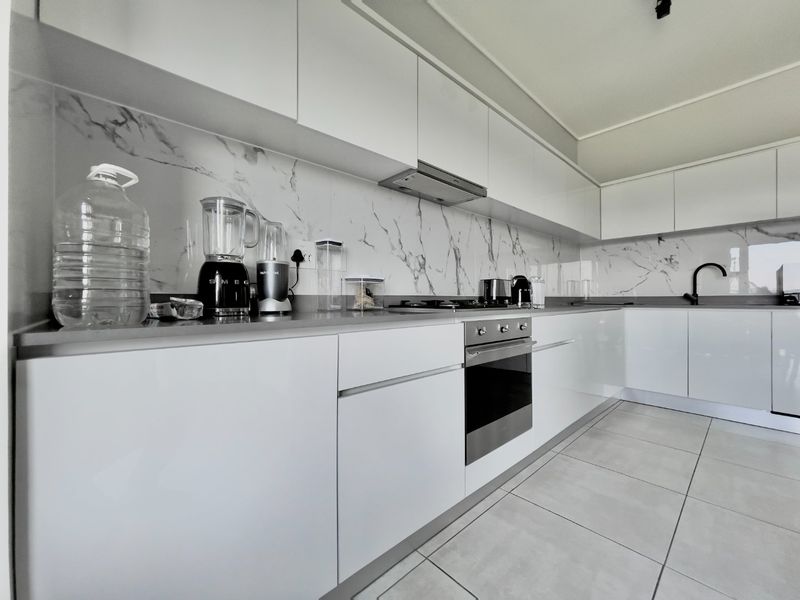 Modern kitchen featuring sleek white cabinetry, marble-look splashbacks, integrated appliances, and high-quality tiled flooring.