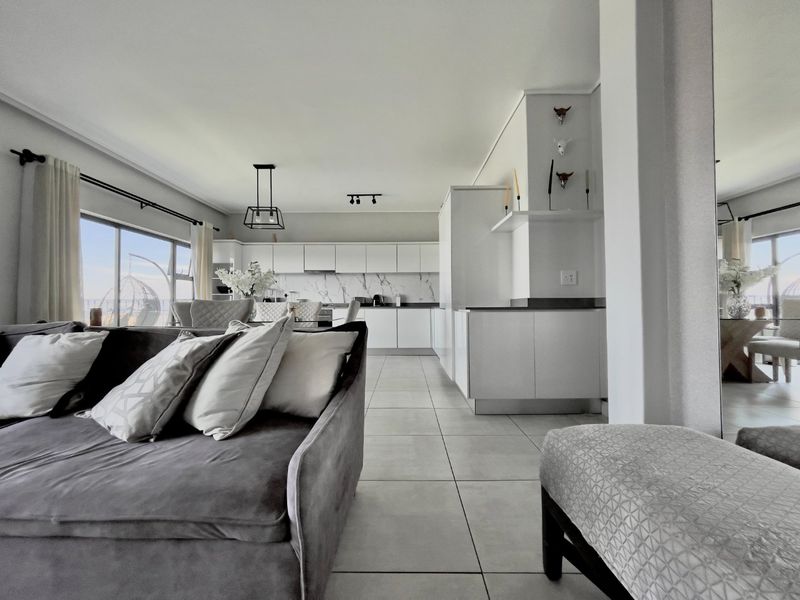 Modern open-plan living and kitchen area featuring sleek white cabinetry, marble-look backsplash, tiled flooring, and large sliding doors leading to an outdoor space.