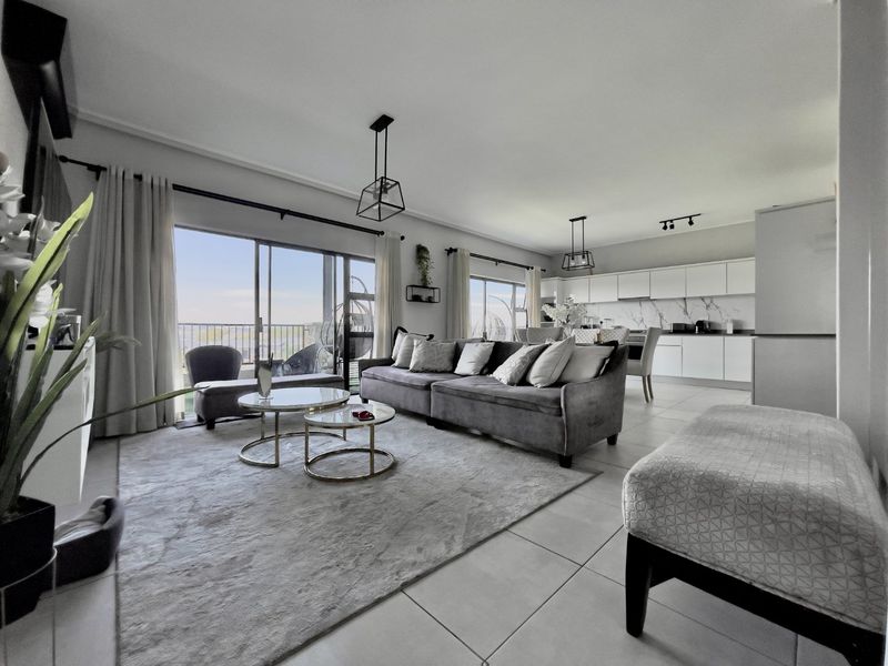 A modern open-plan living and kitchen area featuring sleek white cabinetry, marble-look backsplash, tiled floors, and large sliding doors leading to a balcony.