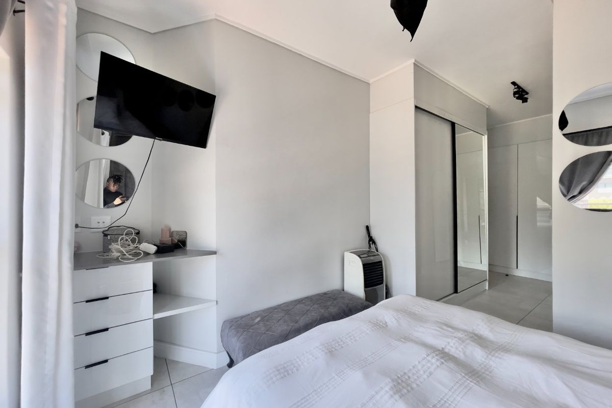 A modern bedroom featuring tiled flooring, built-in cupboards with mirrored sliding doors, and a convenient built-in vanity area.