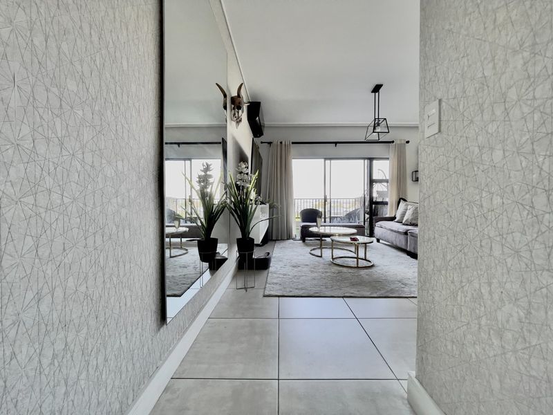 A bright and modern living room featuring large format floor tiles, a full-length wall mirror, and sliding glass doors leading to an outdoor balcony.