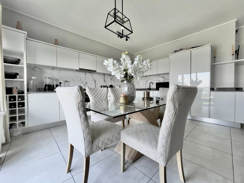 Modern open-plan kitchen and dining area featuring sleek white cabinetry, marble-look splashback, and contemporary pendant lighting with neutral tiled flooring.