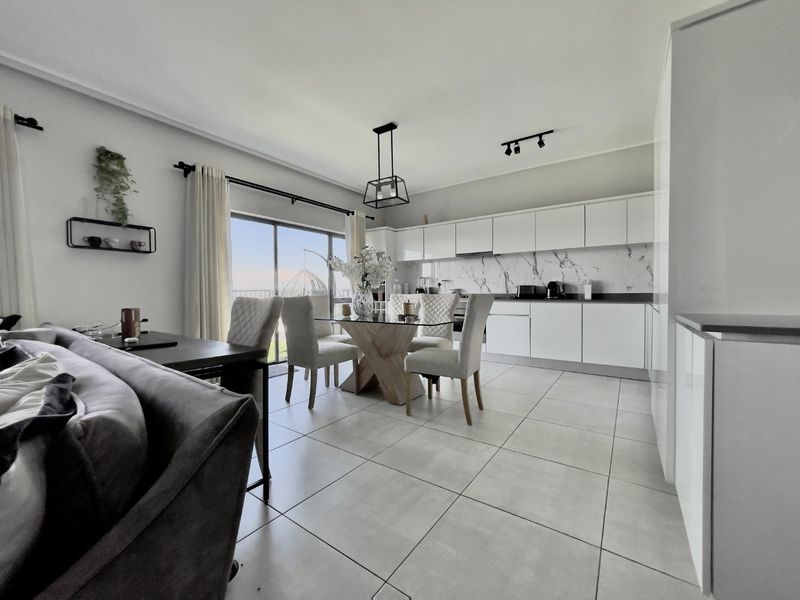 Modern open-plan living and kitchen area featuring sleek white cabinetry, marble-look splashback, large ceramic floor tiles, and direct access to a balcony.