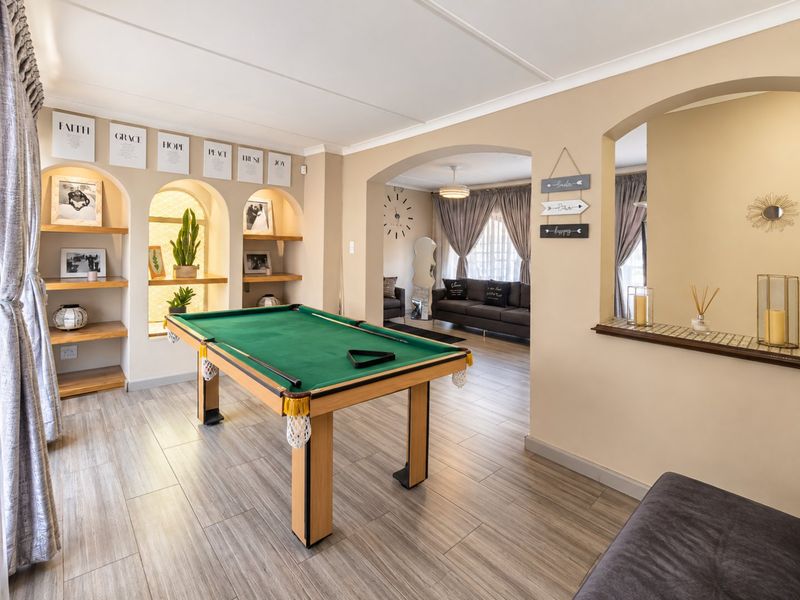 Spacious living area featuring built-in arched shelving, tiled flooring, and an open-plan layout connecting to an adjacent lounge space.