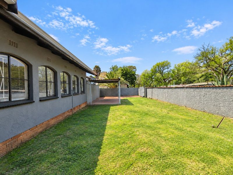 Spacious rear garden featuring a well-maintained lawn, perimeter walling, and a covered patio area adjacent to the house with arched window detailing.