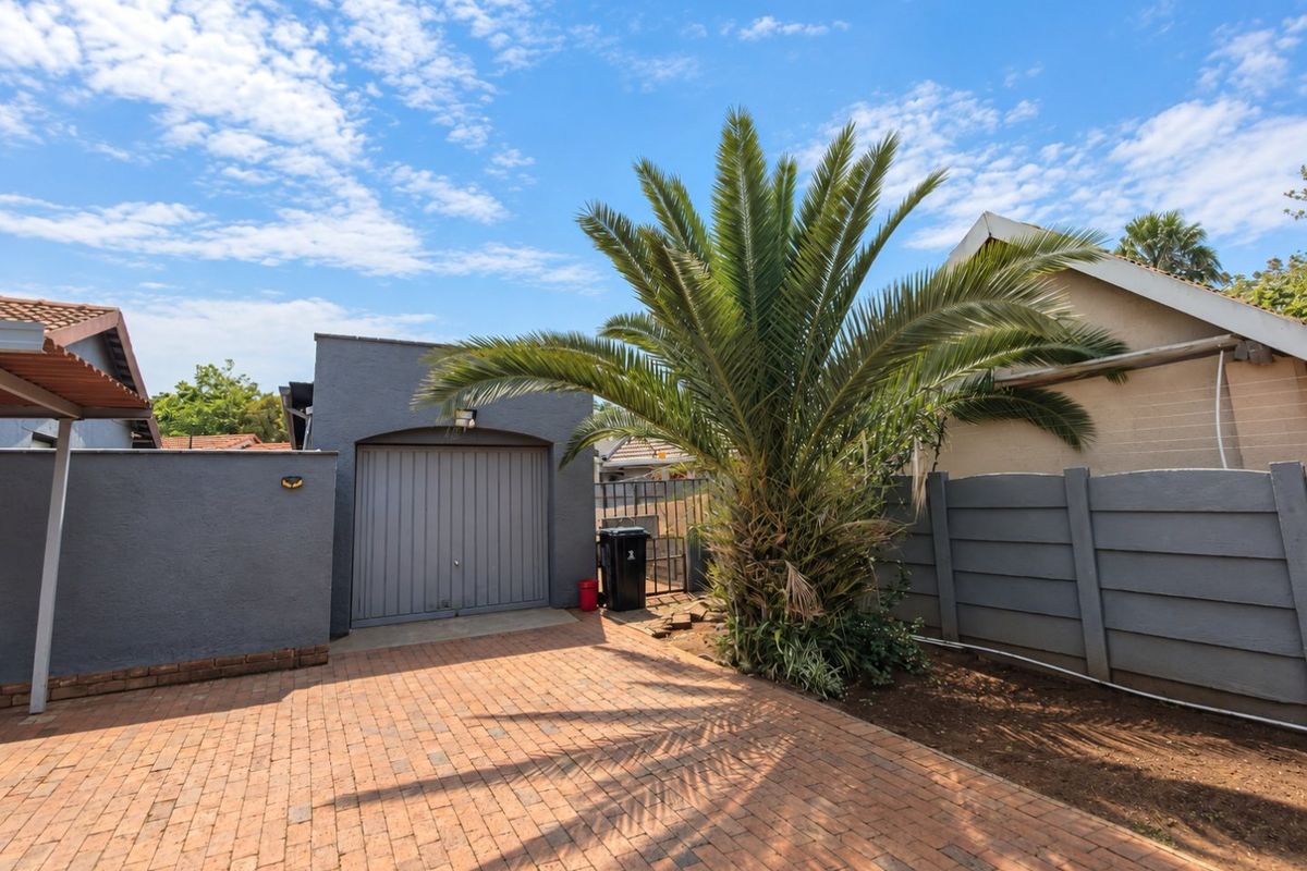 Rear exterior view featuring a paved driveway, a single garage, and a secure boundary wall with established landscaping.