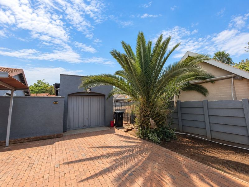 Rear exterior view featuring a paved driveway, a single garage, and a secure boundary wall with established landscaping.