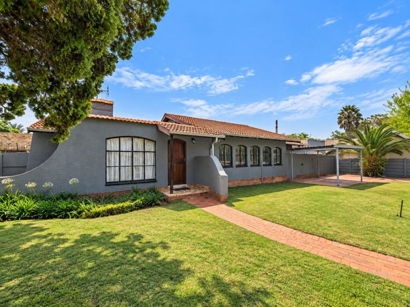 A well-maintained single-story home featuring a grey stucco facade, arched windows, a tiled roof, and a paved walkway leading to the entrance.