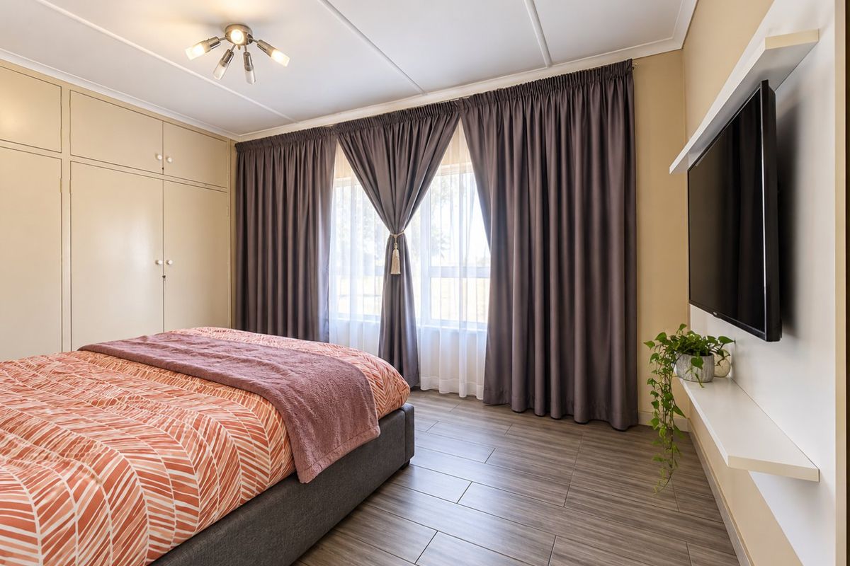 A well-maintained bedroom featuring wood-look tiled flooring, extensive built-in cupboard storage, and a modern floating shelf for media.