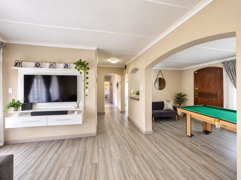 Spacious living area featuring modern laminate flooring, a built-in media console, and an open-plan layout with an elegant archway leading to an adjacent room.