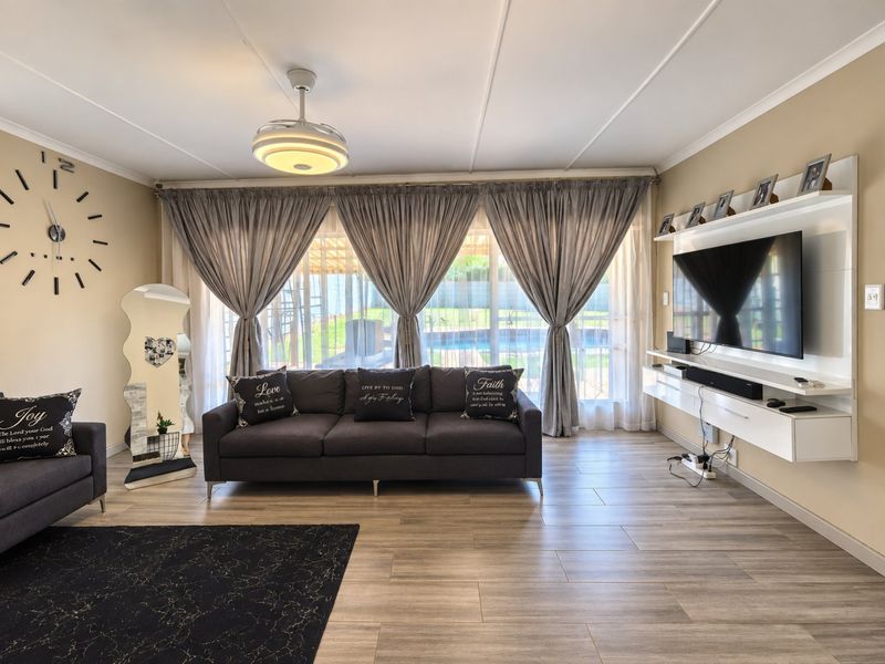A well-maintained living room featuring modern tiled flooring, a built-in media console, and large sliding glass doors providing natural light and garden views.