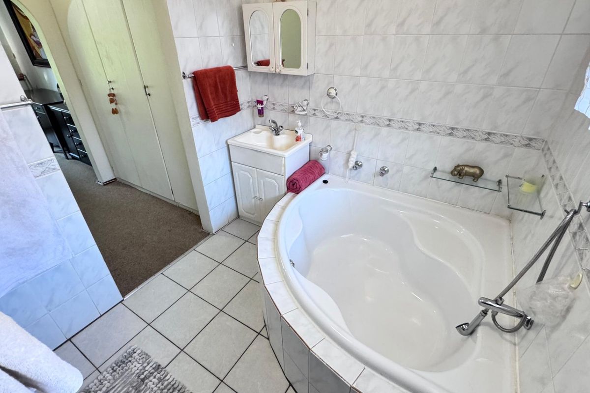 A functional bathroom featuring a corner bathtub, built-in vanity with storage, and tiled finishes throughout.
