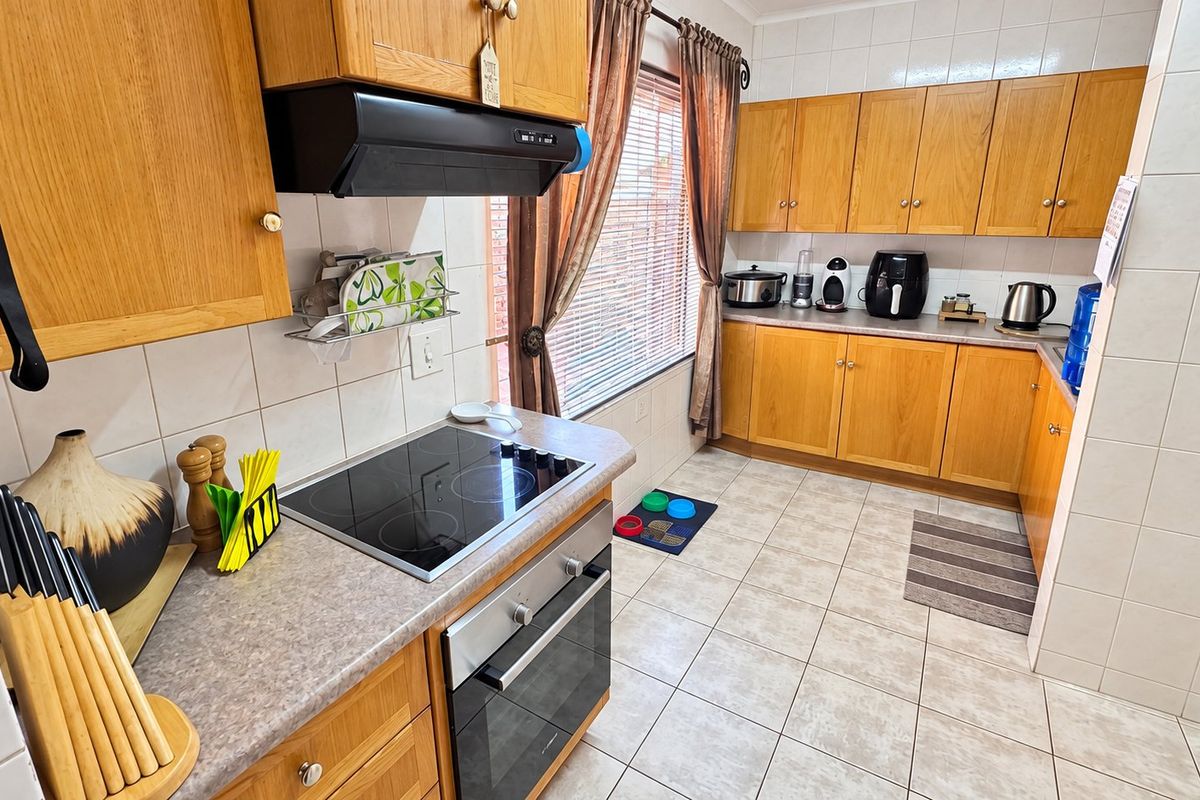 A functional kitchen featuring wood-finish cabinetry, laminate countertops, ceramic tile backsplash, and integrated appliances including an electric hob and oven.