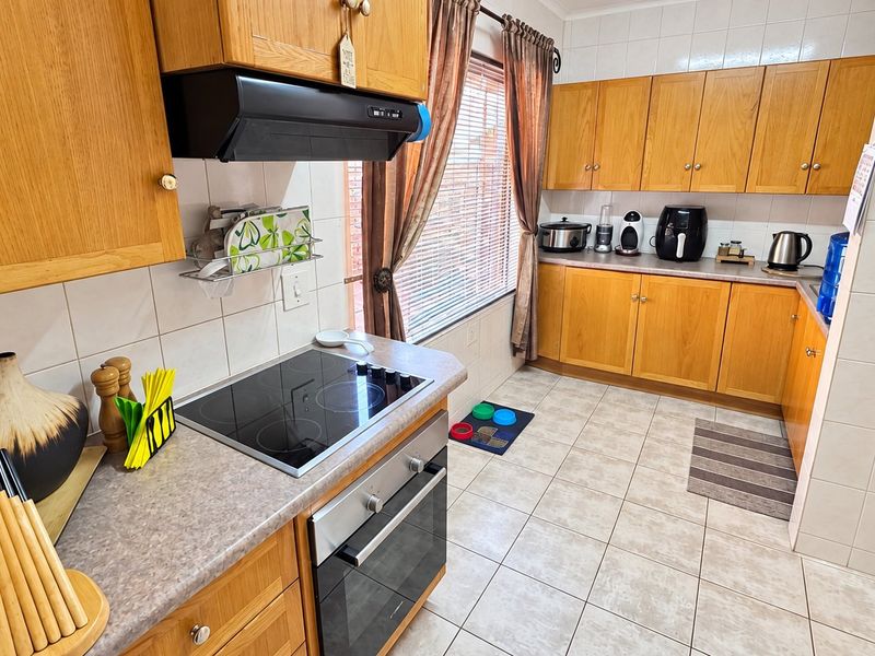 A functional kitchen featuring wood-finish cabinetry, laminate countertops, ceramic tile backsplash, and integrated appliances including an electric hob and oven.