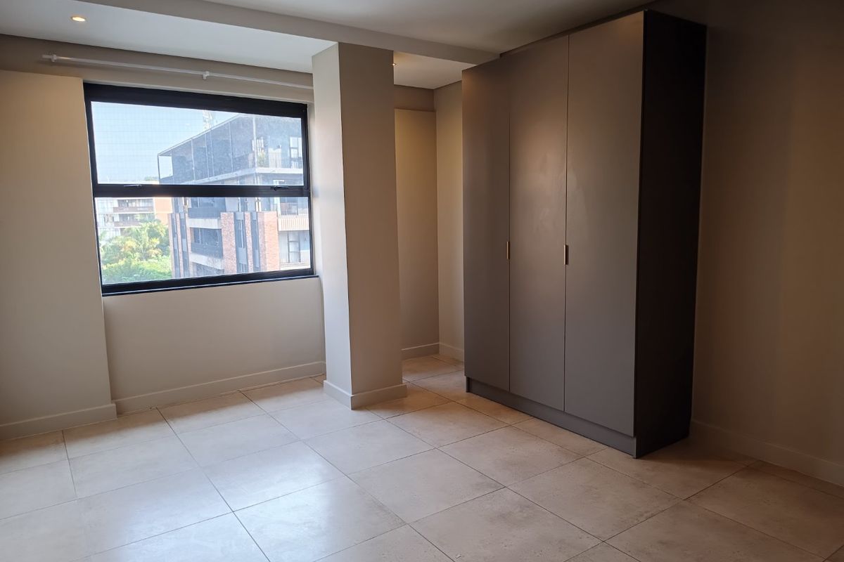 A bright, empty bedroom featuring large format floor tiles, recessed lighting, and a modern built-in wardrobe with a neutral finish.