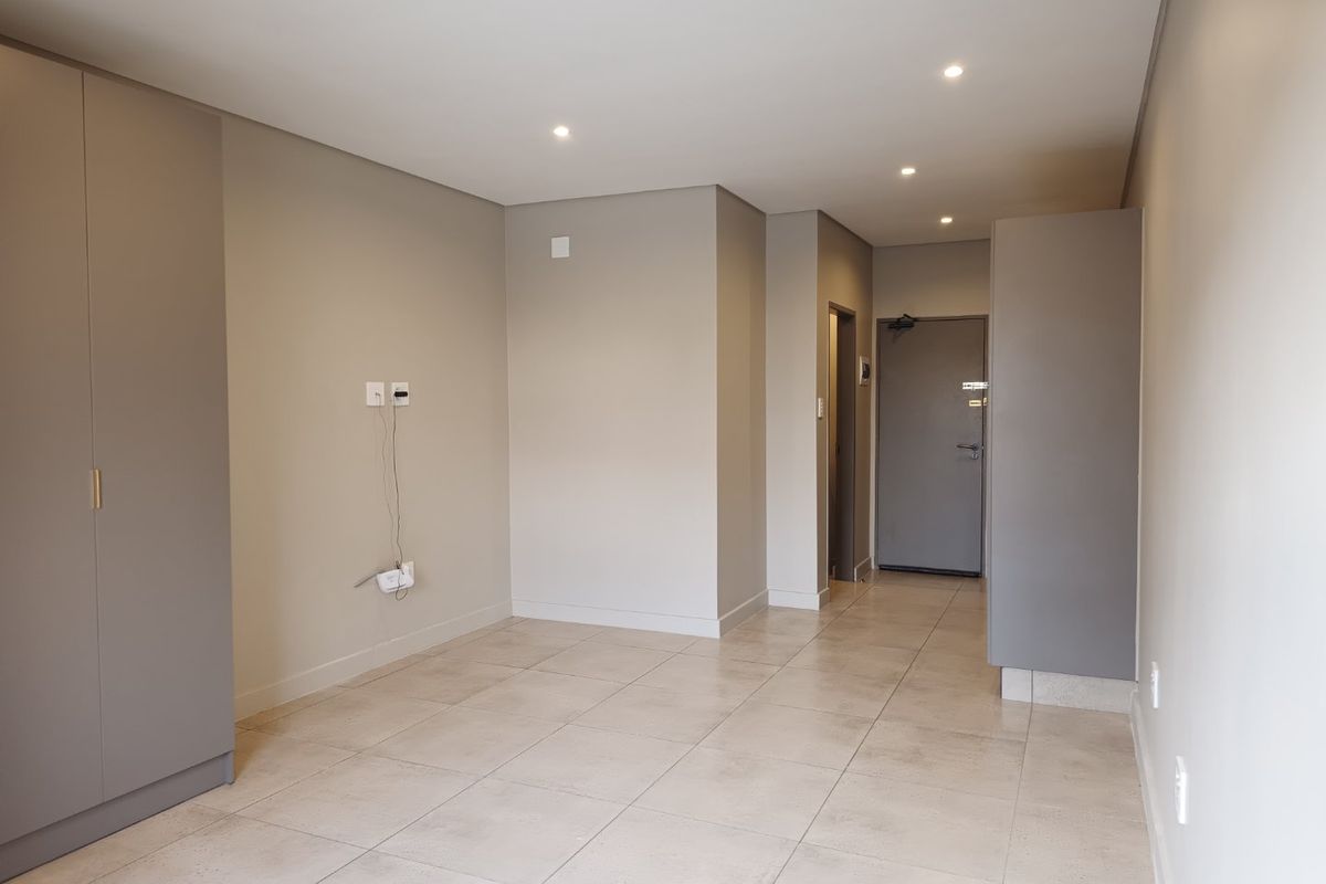 A bright, modern, and empty living area featuring neutral tiled flooring, recessed downlighting, and built-in storage cupboards.