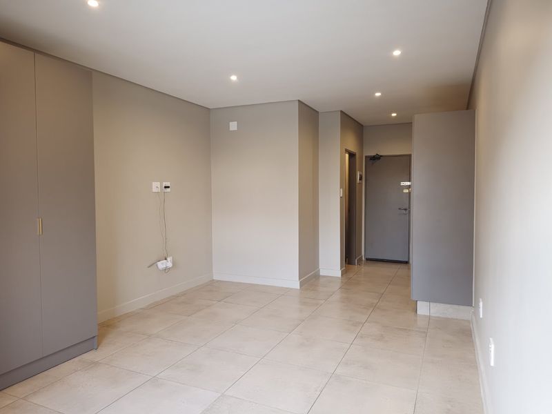 A bright, modern, and empty living area featuring neutral tiled flooring, recessed downlighting, and built-in storage cupboards.