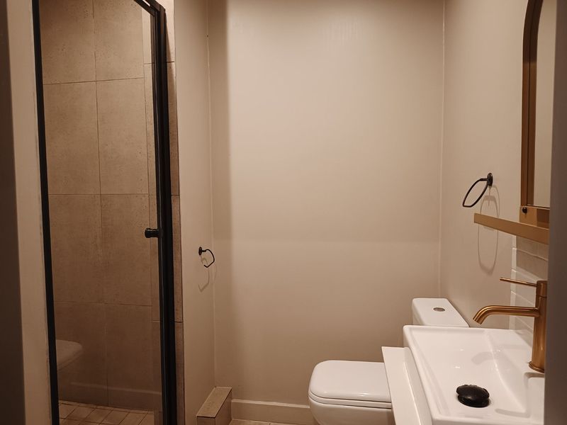 A modern bathroom featuring a glass-enclosed shower, a sleek vanity basin with brass fixtures, and neutral wall finishes.