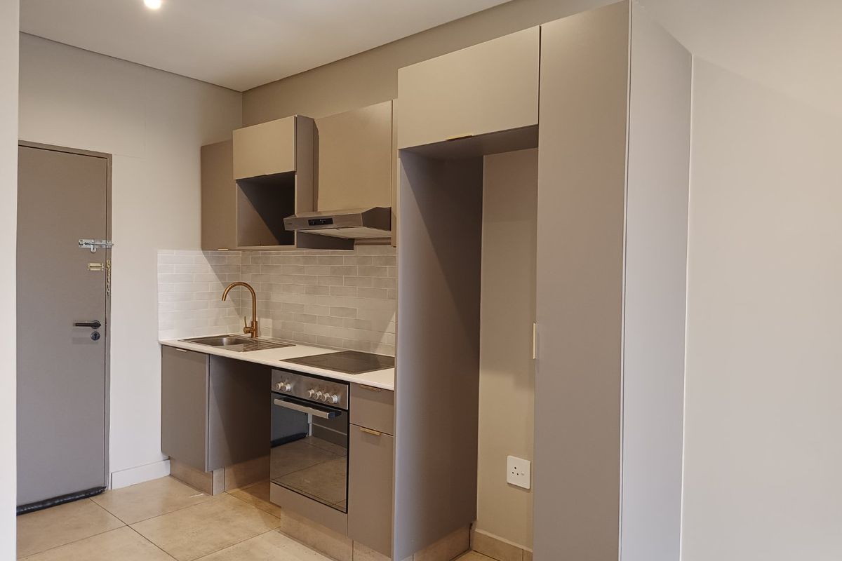 Modern compact kitchen featuring neutral cabinetry, subway tile backsplash, integrated oven and hob, and high-quality brass fixtures.