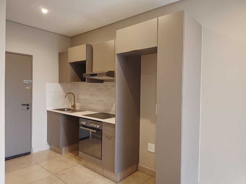 Modern compact kitchen featuring neutral cabinetry, subway tile backsplash, integrated oven and hob, and high-quality brass fixtures.
