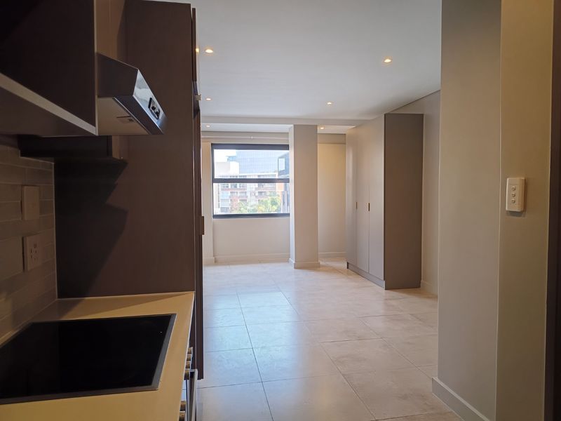 Modern open-plan apartment featuring a sleek kitchen with built-in appliances, tiled flooring, and ample storage, leading into a bright, neutral living area.