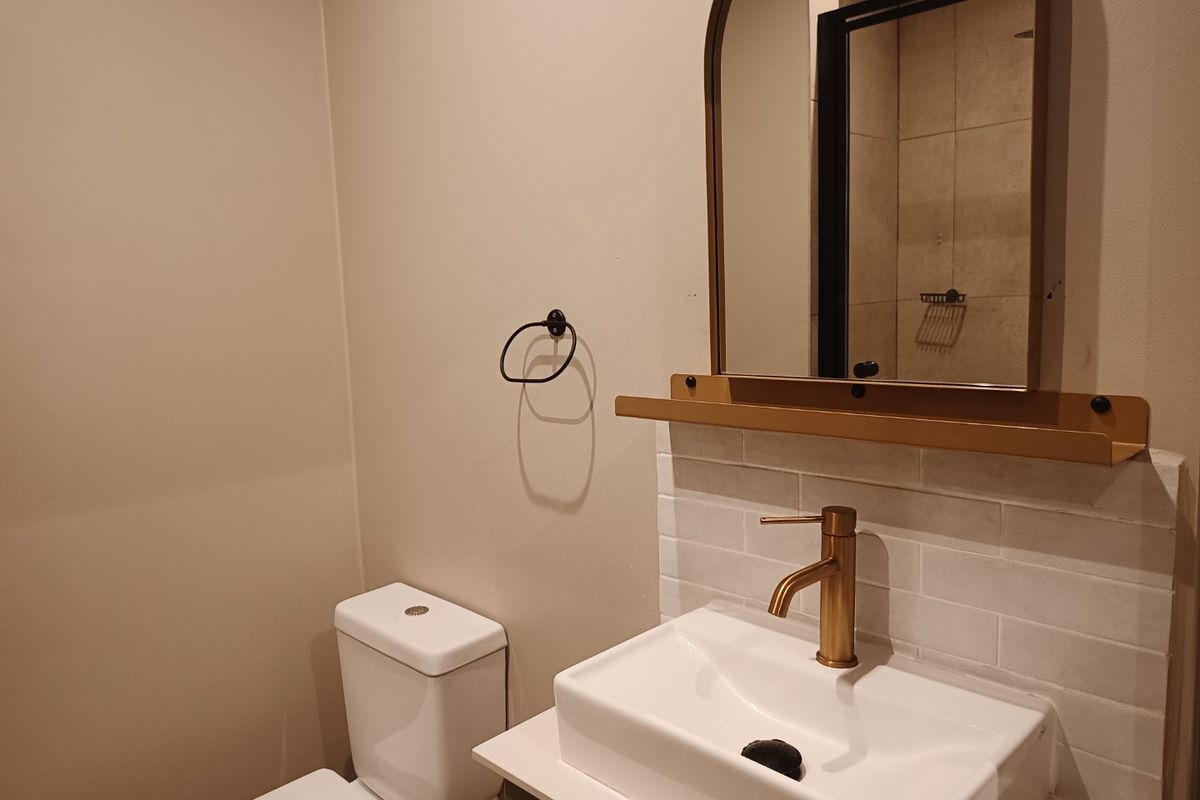 Modern bathroom featuring a vanity with a brass faucet, tiled backsplash, arched mirror with integrated shelf, and a standard toilet.
