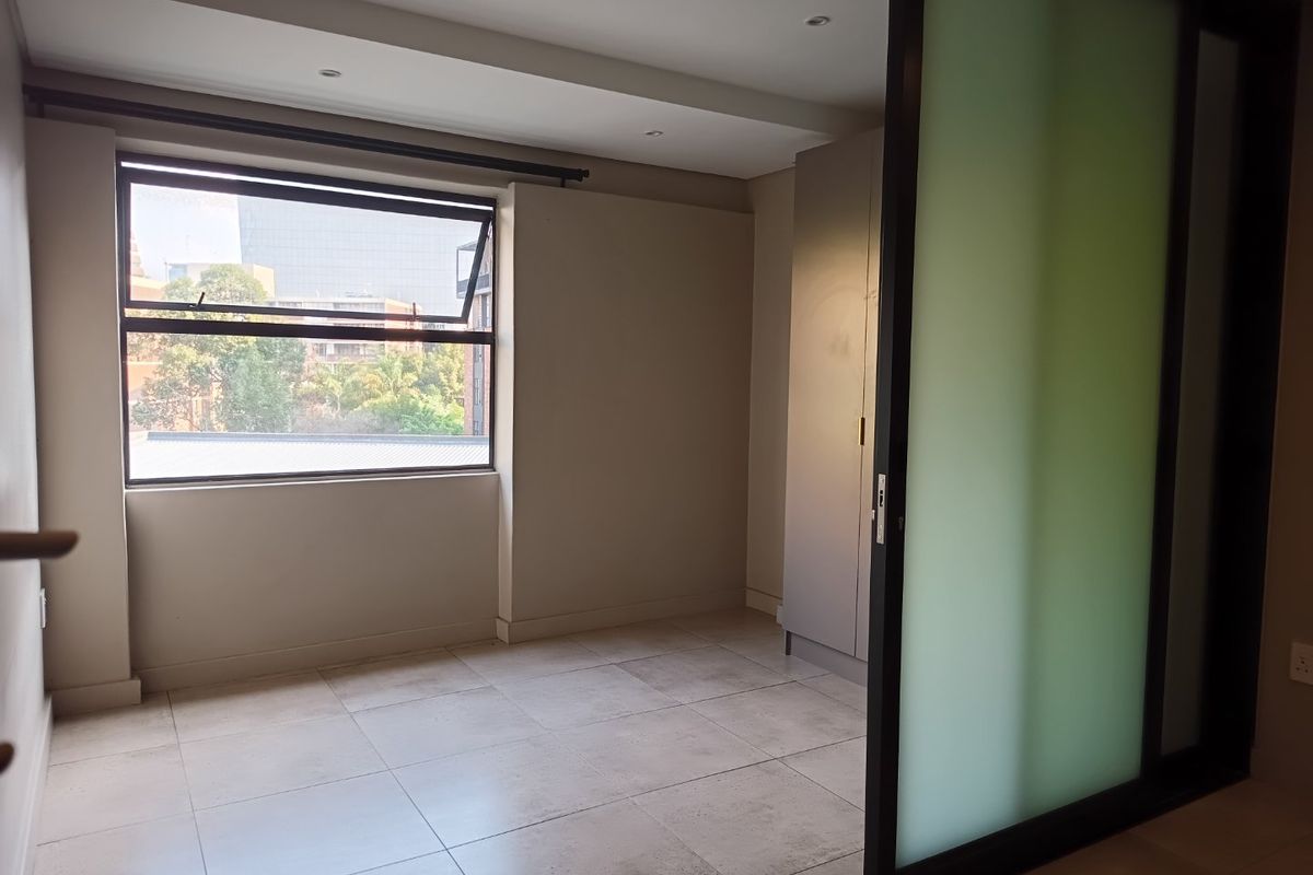 A bright, empty bedroom featuring neutral tiled flooring, a built-in wardrobe, and a modern sliding frosted glass door for privacy.