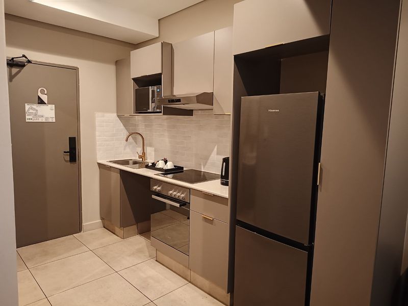 Modern compact kitchen featuring sleek grey cabinetry, stone countertops, brass fixtures, integrated oven, hob, and extractor fan with a tiled backsplash.