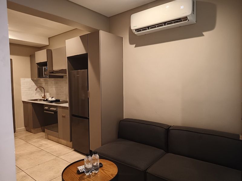 Modern open-plan living area featuring a compact kitchen with built-in cabinetry, integrated appliances, and a wall-mounted air conditioning unit.