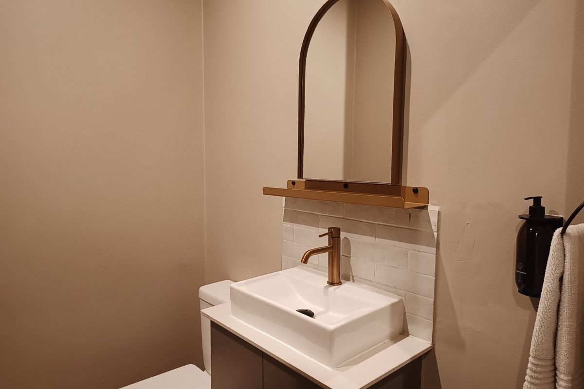 A modern bathroom featuring a vanity with a vessel sink, brass faucet, tiled backsplash, and an arched mirror.