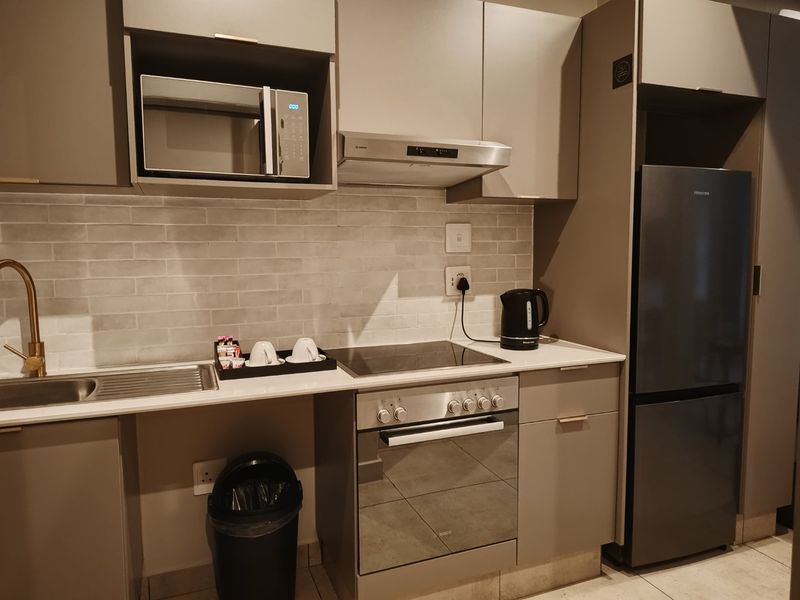 Modern kitchen featuring sleek cabinetry, subway tile backsplash, integrated stainless steel appliances, and a stone countertop with a brass faucet.