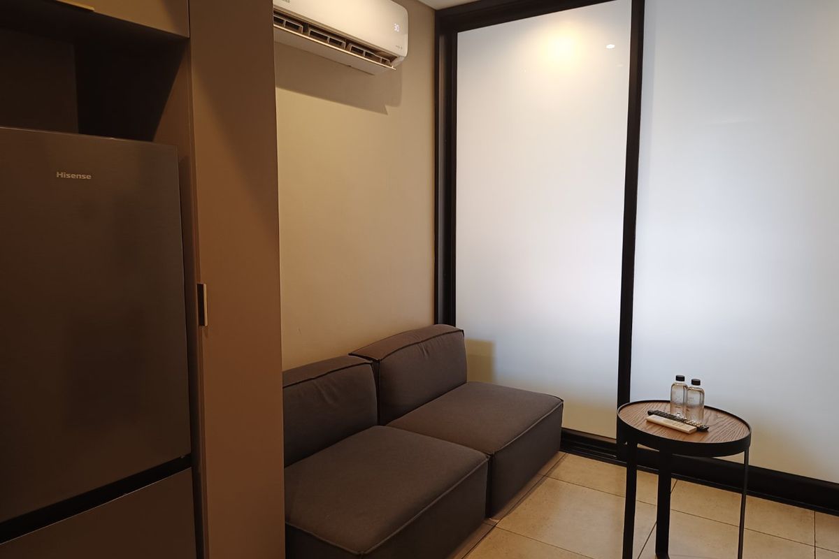 A compact living area featuring tiled flooring, a wall-mounted split-system air conditioner, and a large sliding glass door providing natural light.