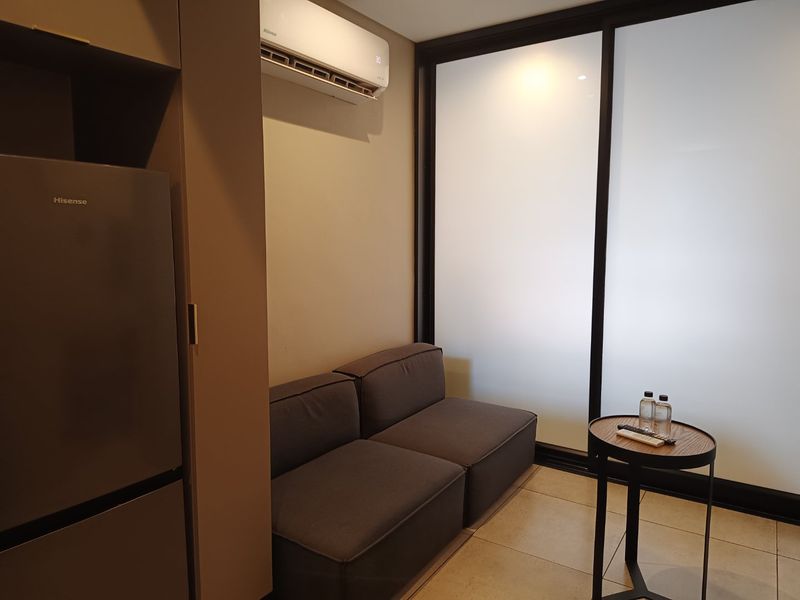 A compact living area featuring tiled flooring, a wall-mounted split-system air conditioner, and a large sliding glass door providing natural light.