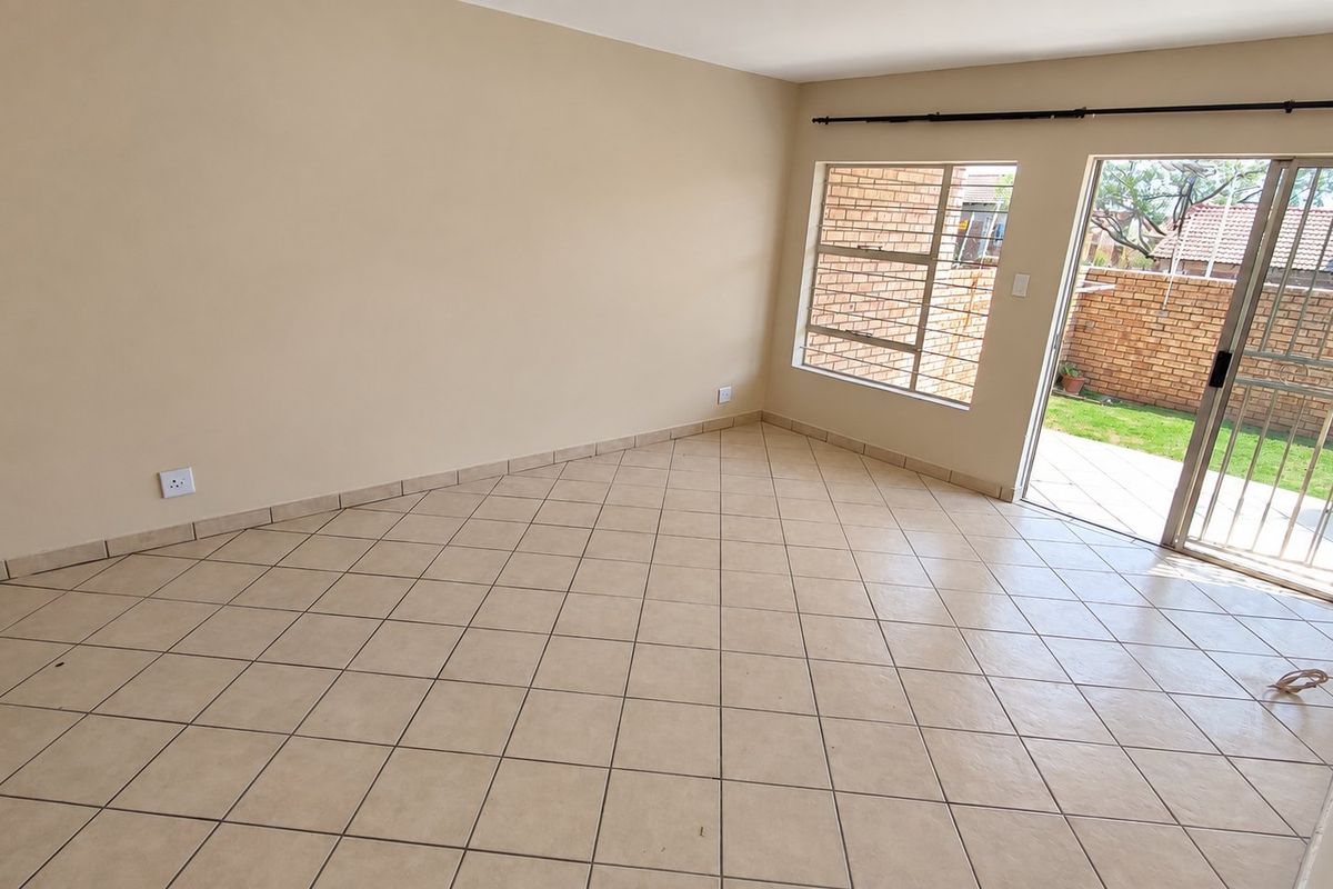 An empty, tiled living room featuring a sliding glass door that provides direct access to the rear patio and garden area.