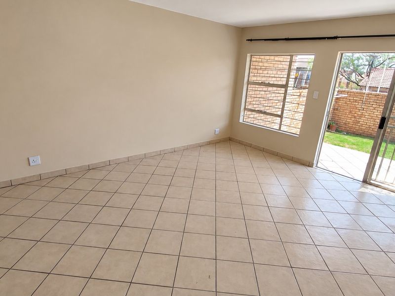 An empty, tiled living room featuring a sliding glass door that provides direct access to the rear patio and garden area.