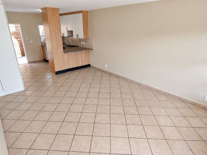 An open-plan living and kitchen area featuring neutral tiled flooring, built-in cabinetry, and a functional kitchen layout in a townhouse setting.