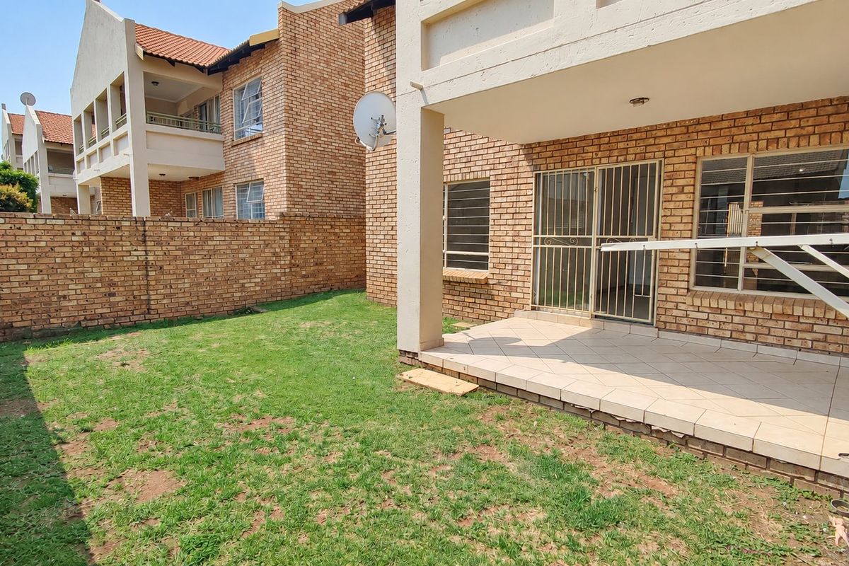 Rear view of the townhouse featuring a private garden, a tiled patio area, and secure access through a sliding door with a security gate.