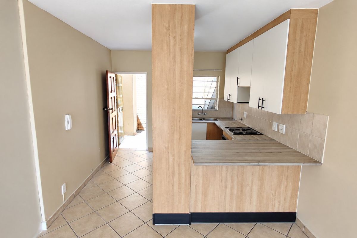 A functional kitchen featuring light wood-look cabinetry, laminate countertops, a gas hob, and tiled flooring, with direct access to an exterior area.