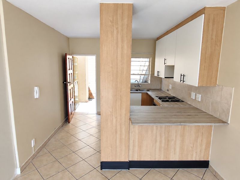 A functional kitchen featuring light wood-look cabinetry, laminate countertops, a gas hob, and tiled flooring, with direct access to an exterior area.