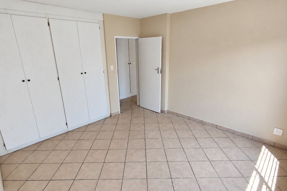 An empty bedroom featuring neutral wall paint, tiled flooring, and built-in cupboards, offering a clean and versatile space.