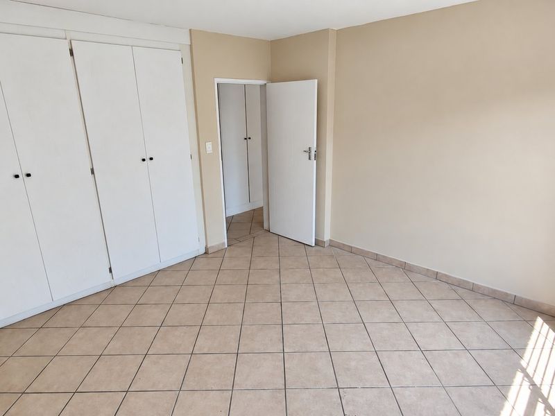 An empty bedroom featuring neutral wall paint, tiled flooring, and built-in cupboards, offering a clean and versatile space.