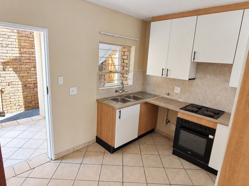 A functional kitchen featuring built-in cabinetry, a double sink, an electric hob, and an oven, with direct access to an outdoor patio area.