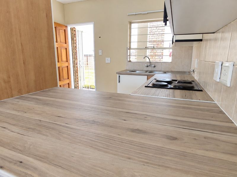 A functional kitchen featuring wood-look laminate countertops, a built-in electric hob, tiled backsplash, and direct access to the exterior.