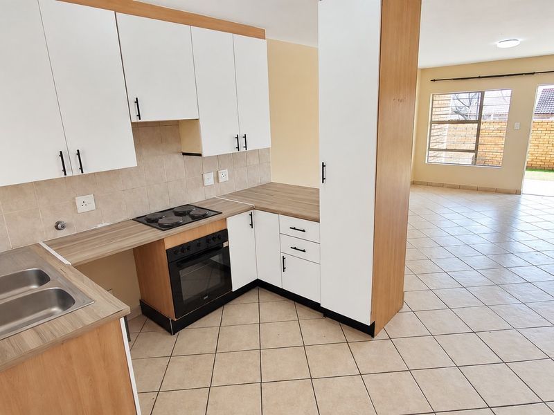 Open-plan kitchen and living area featuring white cabinetry, laminate countertops, built-in oven and hob, tiled flooring, and access to the rear garden.