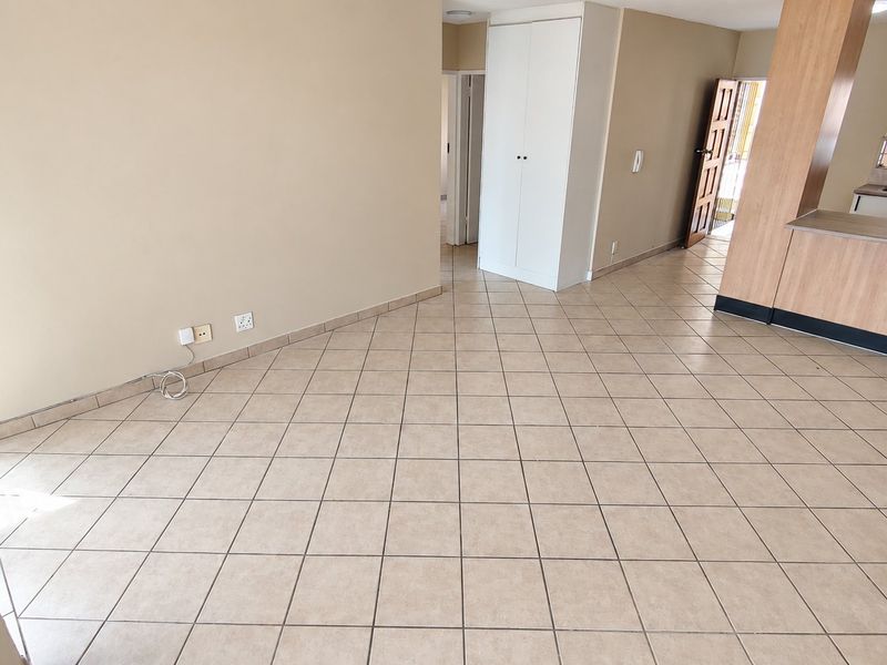 Spacious open-plan living area featuring neutral tiled flooring, a built-in cupboard, and an adjoining kitchen with functional cabinetry and built-in appliances.