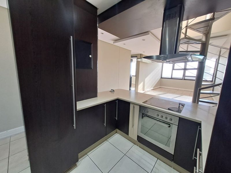Modern kitchen featuring dark cabinetry, stone countertops, integrated appliances, and a striking spiral staircase leading to the upper level.