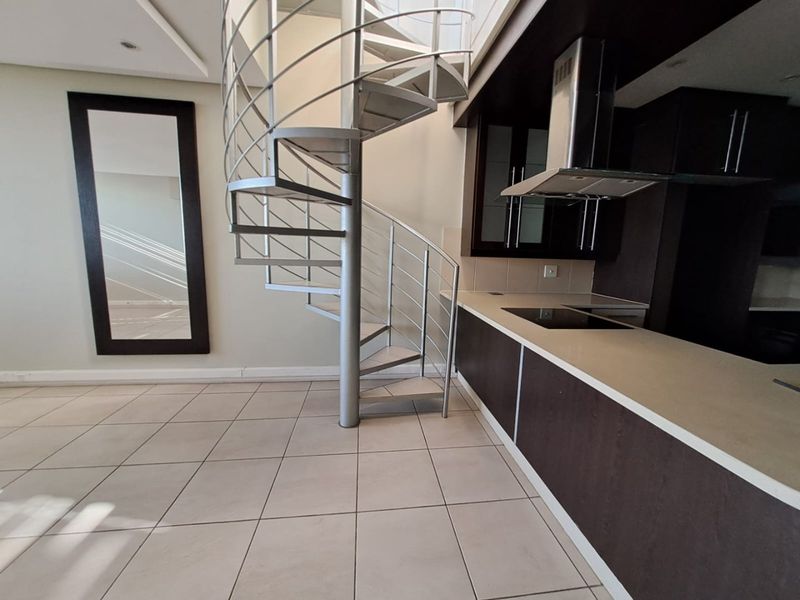 Open-plan living area featuring a modern spiral staircase, tiled flooring, and a contemporary kitchen with built-in cabinetry, hob, and extractor fan.