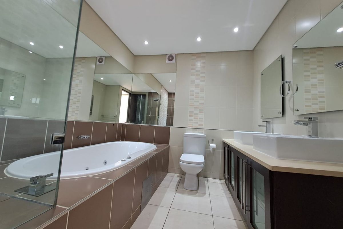 Modern bathroom featuring a built-in bathtub, dual vanity with vessel sinks, glass shower screen, and neutral tiled finishes throughout.